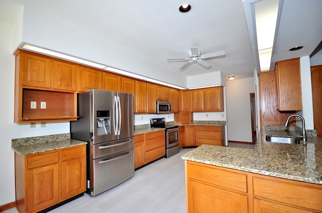 kitchen featuring brown cabinetry, light stone counters, a peninsula, stainless steel appliances, and a sink