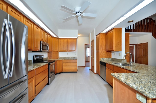 kitchen with light wood finished floors, appliances with stainless steel finishes, brown cabinets, light stone counters, and a sink