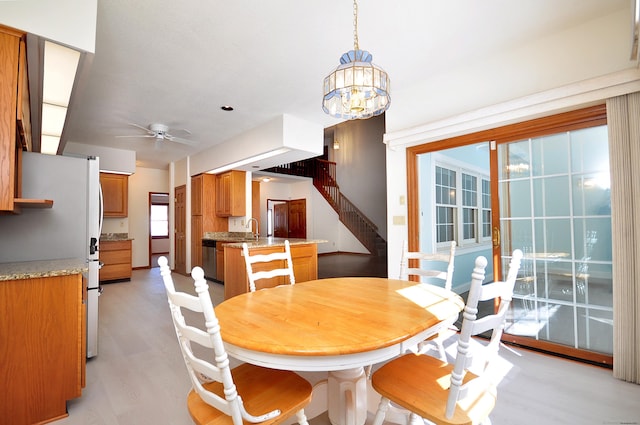 dining space featuring light wood finished floors, stairs, and ceiling fan with notable chandelier