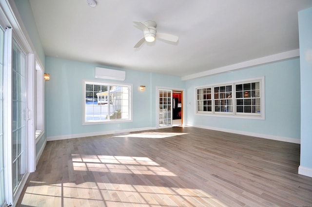 interior space with wood finished floors, ceiling fan, baseboards, and a wall mounted AC