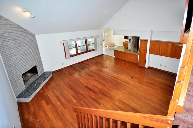 unfurnished living room with dark wood-style flooring, a fireplace, vaulted ceiling, track lighting, and baseboards