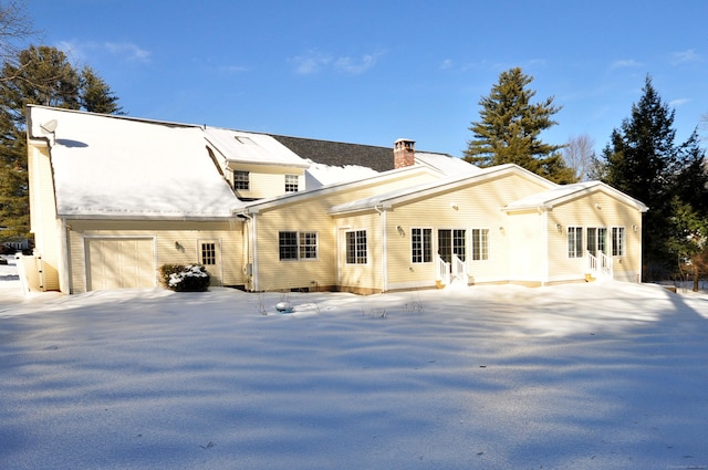 snow covered back of property featuring a garage and a chimney