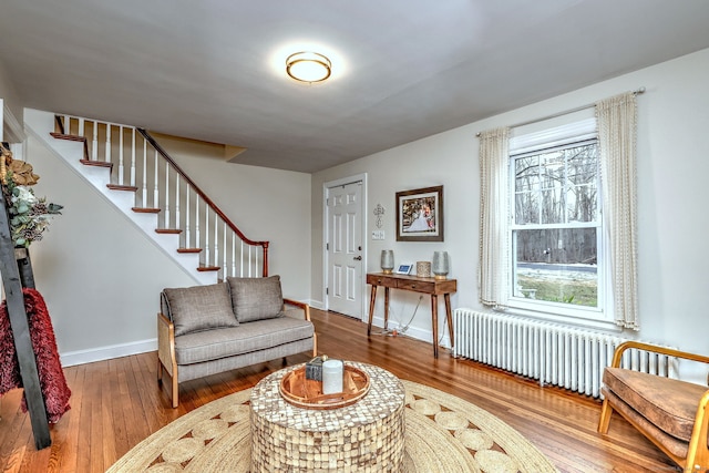 living area with baseboards, stairway, wood-type flooring, and radiator