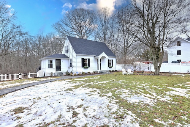 cape cod house featuring a shingled roof, entry steps, fence, and a lawn