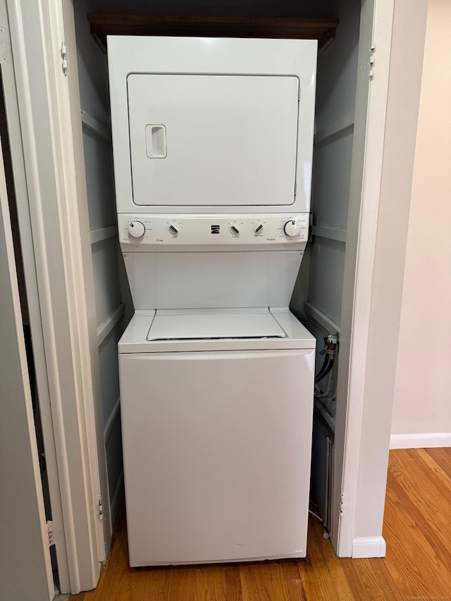 clothes washing area with stacked washer / dryer, laundry area, baseboards, and wood finished floors