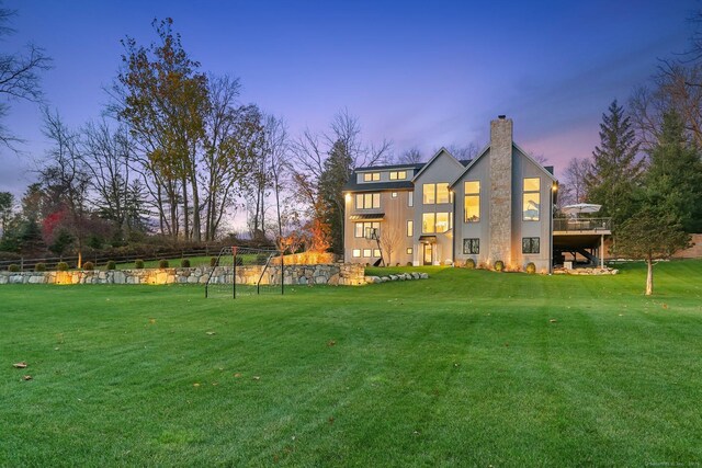 rear view of property featuring a wooden deck, a chimney, and a yard