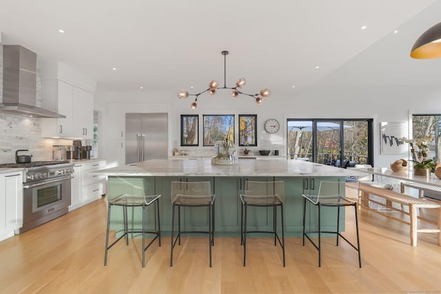 kitchen featuring white cabinets, premium appliances, a large island, wall chimney exhaust hood, and light wood-type flooring