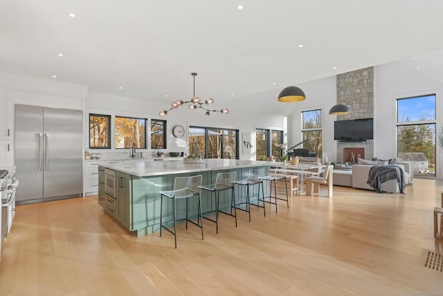 kitchen with light wood finished floors, white cabinets, a spacious island, a breakfast bar, and built in appliances