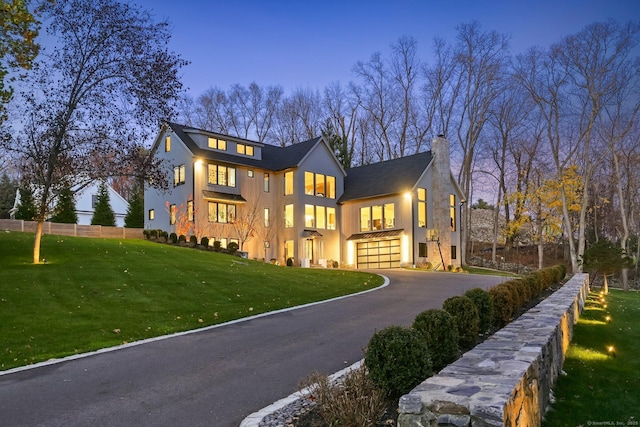 view of front of house featuring aphalt driveway, an attached garage, fence, a front lawn, and a chimney