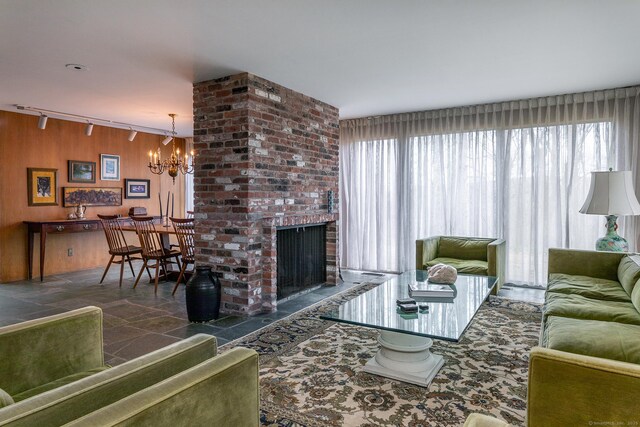 living area with wooden walls, rail lighting, stone finish flooring, a brick fireplace, and a chandelier