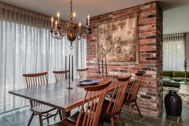 dining area featuring brick wall, plenty of natural light, and an inviting chandelier