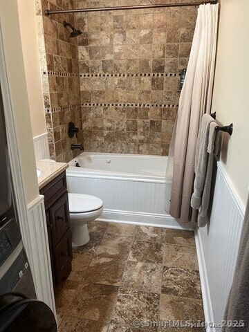 bathroom with stacked washing maching and dryer, shower / bathtub combination with curtain, a wainscoted wall, and vanity