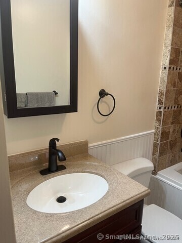 full bathroom with toilet, wainscoting, bathing tub / shower combination, and vanity