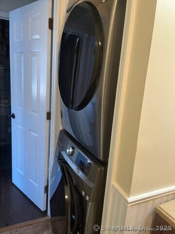 washroom with stacked washer and clothes dryer, wainscoting, and laundry area