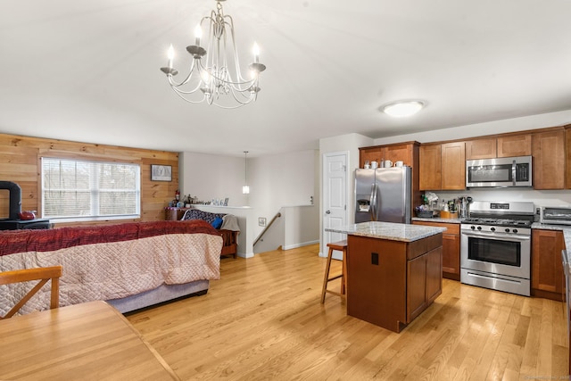 kitchen featuring stainless steel appliances, a kitchen island, open floor plan, brown cabinets, and light wood finished floors