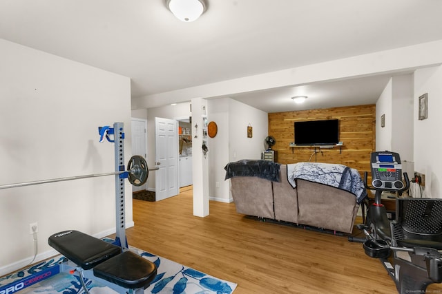 exercise room with an accent wall, light wood-type flooring, wood walls, and baseboards