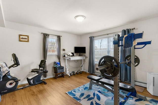 workout room featuring a baseboard heating unit, plenty of natural light, wood finished floors, and baseboards