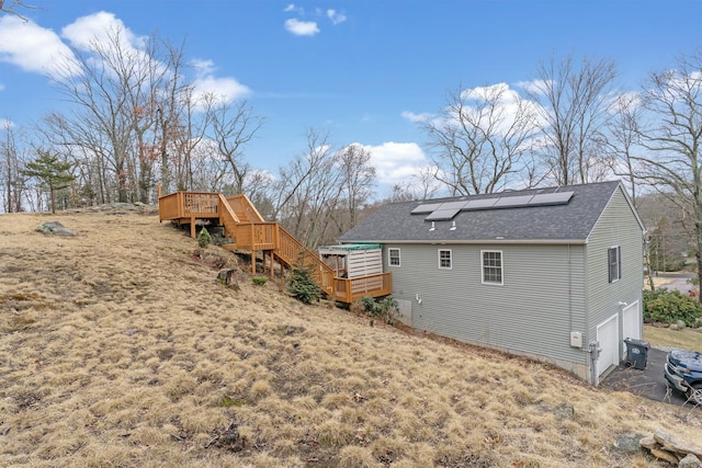 back of house featuring a garage, roof with shingles, a deck, and solar panels