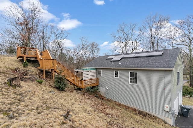 view of side of home featuring a deck, solar panels, a shingled roof, and stairs