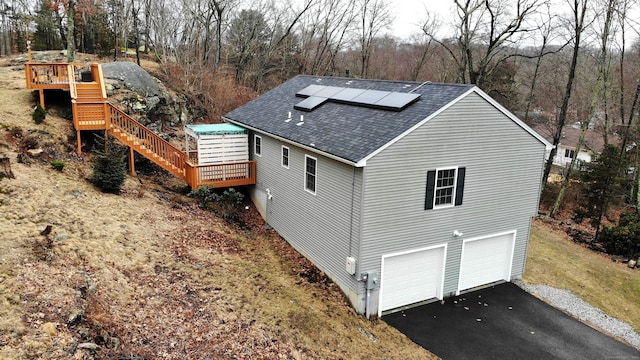 view of home's exterior featuring aphalt driveway, a garage, solar panels, roof with shingles, and a wooden deck