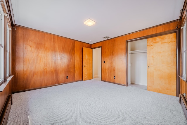 unfurnished bedroom featuring carpet, visible vents, a baseboard heating unit, and wood walls