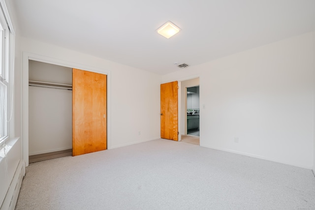 unfurnished bedroom featuring baseboards, a closet, a baseboard heating unit, and carpet flooring