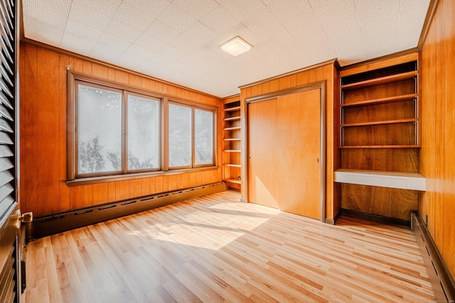 spare room featuring built in shelves, wooden walls, a baseboard heating unit, and wood finished floors