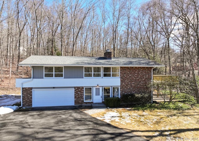 view of front facade featuring a garage, brick siding, a chimney, and aphalt driveway