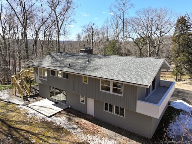 rear view of property featuring a shingled roof, dirt driveway, a chimney, and stairs