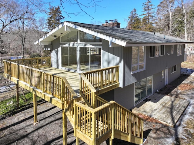 rear view of property featuring a shingled roof, a chimney, and a deck