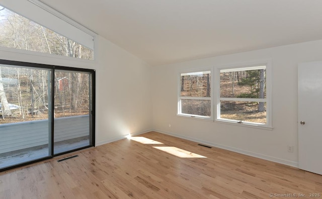 empty room featuring visible vents, vaulted ceiling, baseboards, and wood finished floors