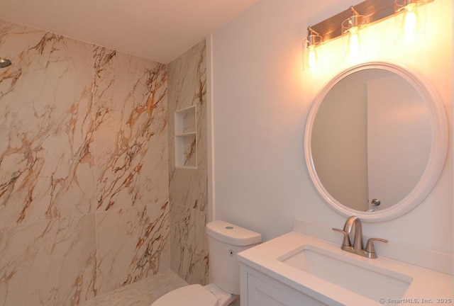 full bathroom with a tile shower, vanity, and toilet