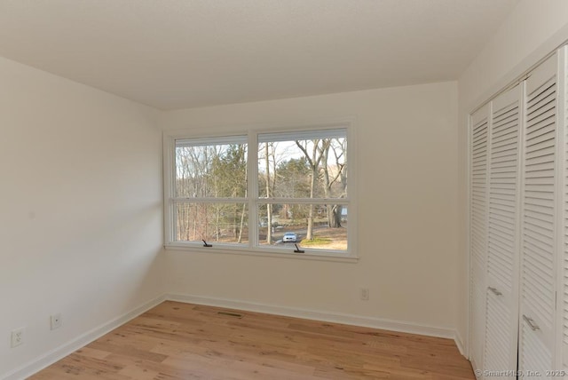 unfurnished bedroom with light wood-type flooring, a closet, and baseboards