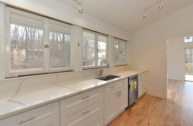 kitchen with white cabinets, light stone counters, a sink, vaulted ceiling, and stainless steel dishwasher