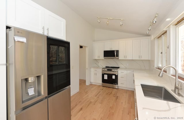 kitchen featuring stainless steel appliances, a sink, white cabinets, vaulted ceiling, and light wood finished floors