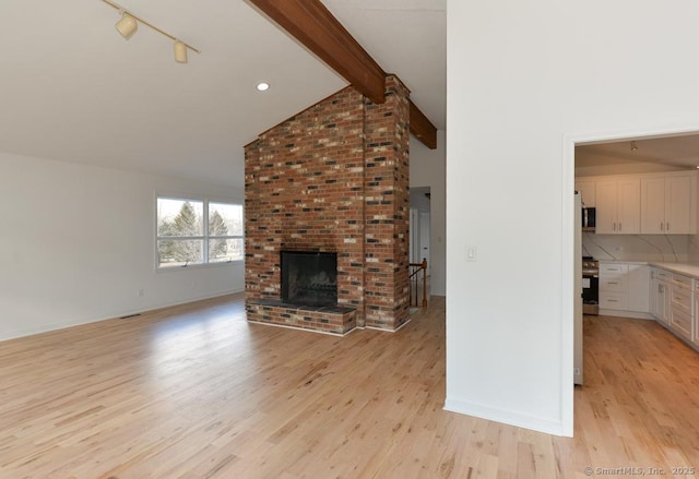 unfurnished living room featuring lofted ceiling with beams, light wood-style floors, a fireplace, and baseboards