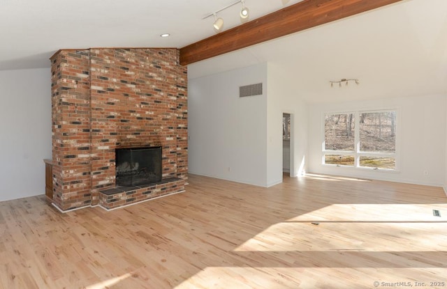 unfurnished living room with vaulted ceiling with beams, wood finished floors, visible vents, a brick fireplace, and track lighting