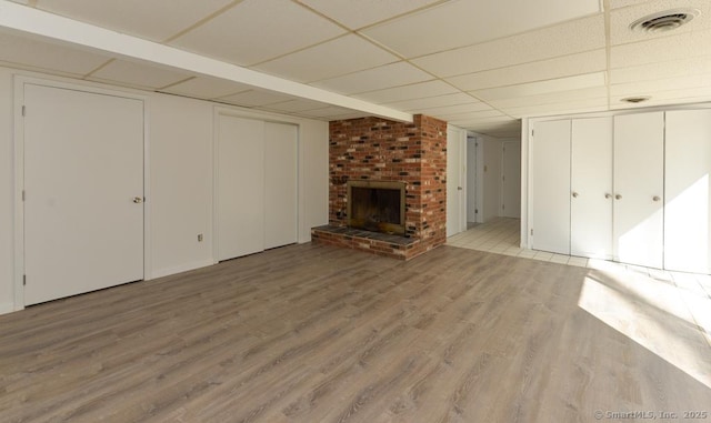 unfurnished living room with a drop ceiling, light wood-type flooring, visible vents, and a brick fireplace