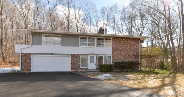 view of front facade with an attached garage, a chimney, aphalt driveway, and brick siding