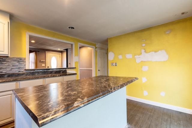 kitchen featuring dark wood-style flooring, decorative backsplash, white cabinets, a kitchen island, and baseboards