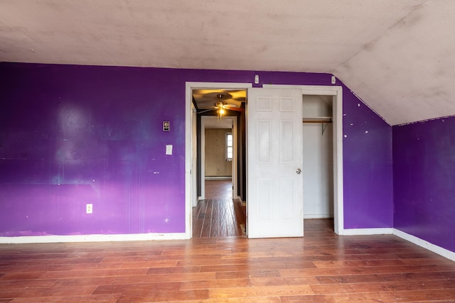 unfurnished bedroom featuring lofted ceiling, a baseboard radiator, wood finished floors, and baseboards