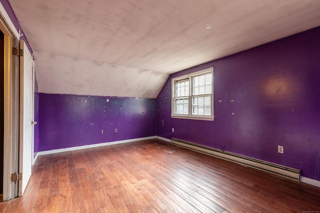 additional living space with vaulted ceiling, a baseboard radiator, hardwood / wood-style flooring, and baseboards