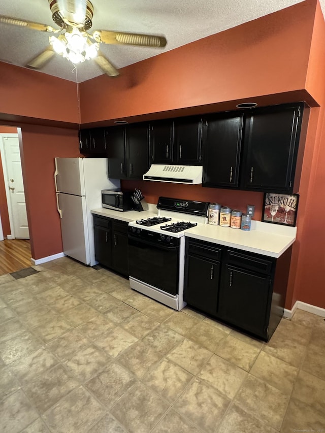 kitchen featuring dark cabinets, exhaust hood, freestanding refrigerator, stainless steel microwave, and gas stove