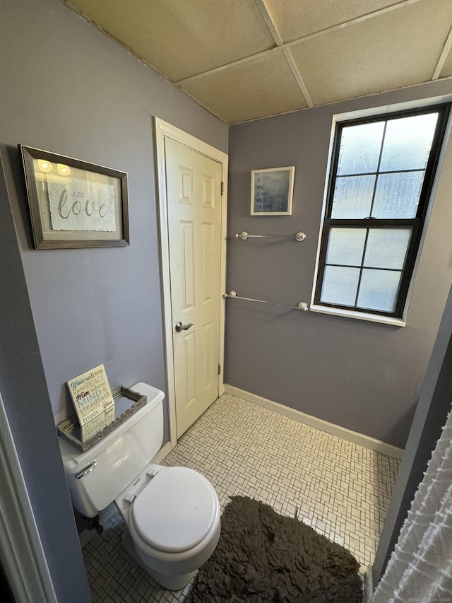 bathroom featuring toilet, baseboards, a paneled ceiling, and tile patterned floors