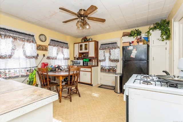 kitchen with light floors, white microwave, a ceiling fan, freestanding refrigerator, and gas range