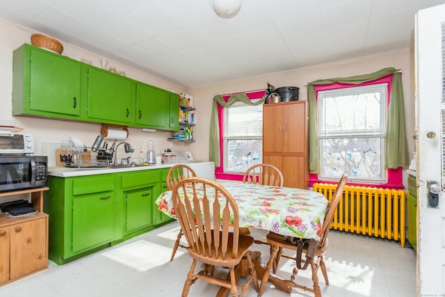 kitchen featuring radiator, light floors, black microwave, and green cabinetry