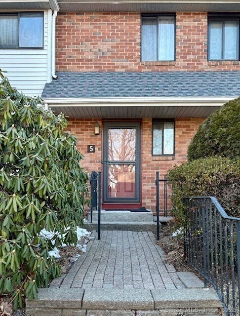 entrance to property featuring a shingled roof and brick siding