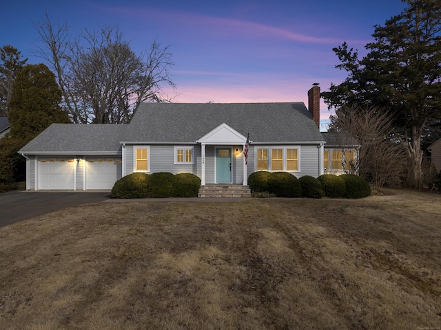 view of front facade featuring driveway, a chimney, roof with shingles, an attached garage, and a front yard