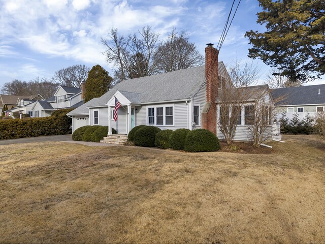 view of front of property with an attached garage, a shingled roof, a residential view, a chimney, and a front yard