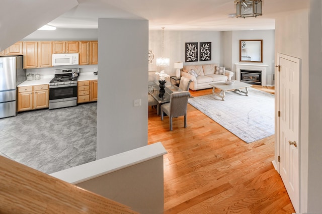 kitchen with light countertops, appliances with stainless steel finishes, light brown cabinetry, a glass covered fireplace, and an inviting chandelier